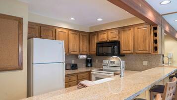 A kitchen with wooden cabinets, a refrigerator, a microwave, a toaster, and a sink.