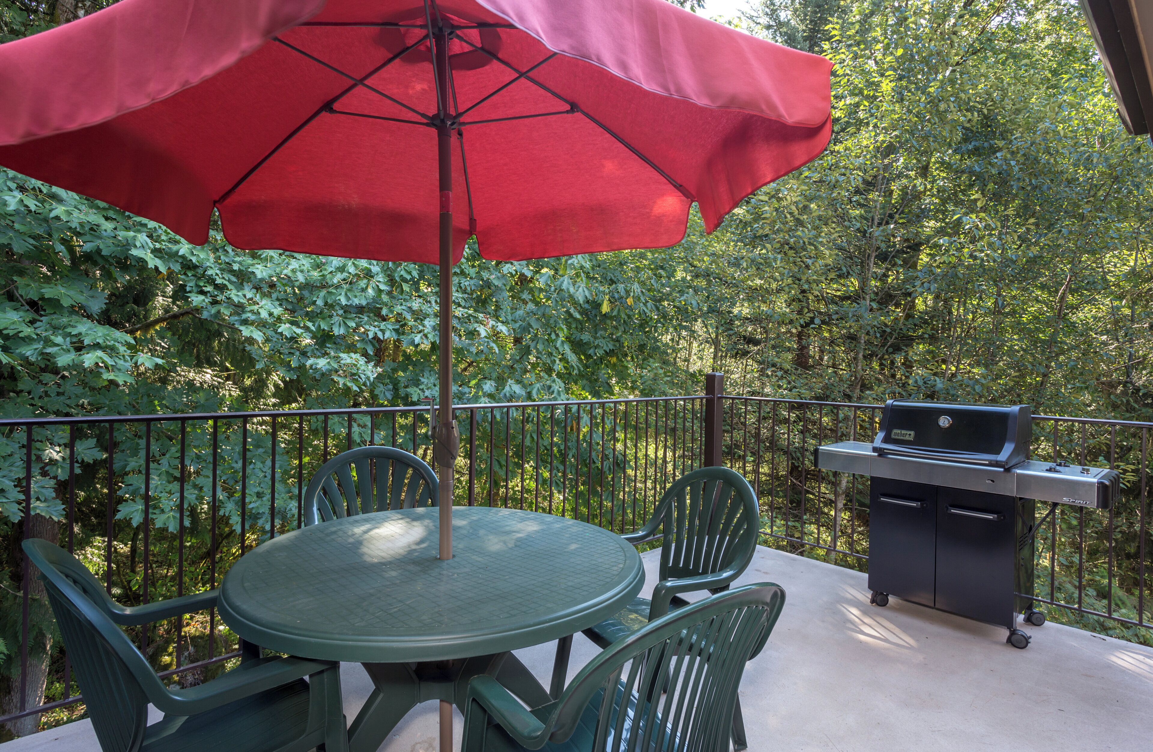 An outdoor patio with a round table and chairs, a red umbrella, and a grill.
