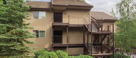 A two-story residential building with a central staircase, a covered front porch, and a landscaped front yard with shrubs and a tree.