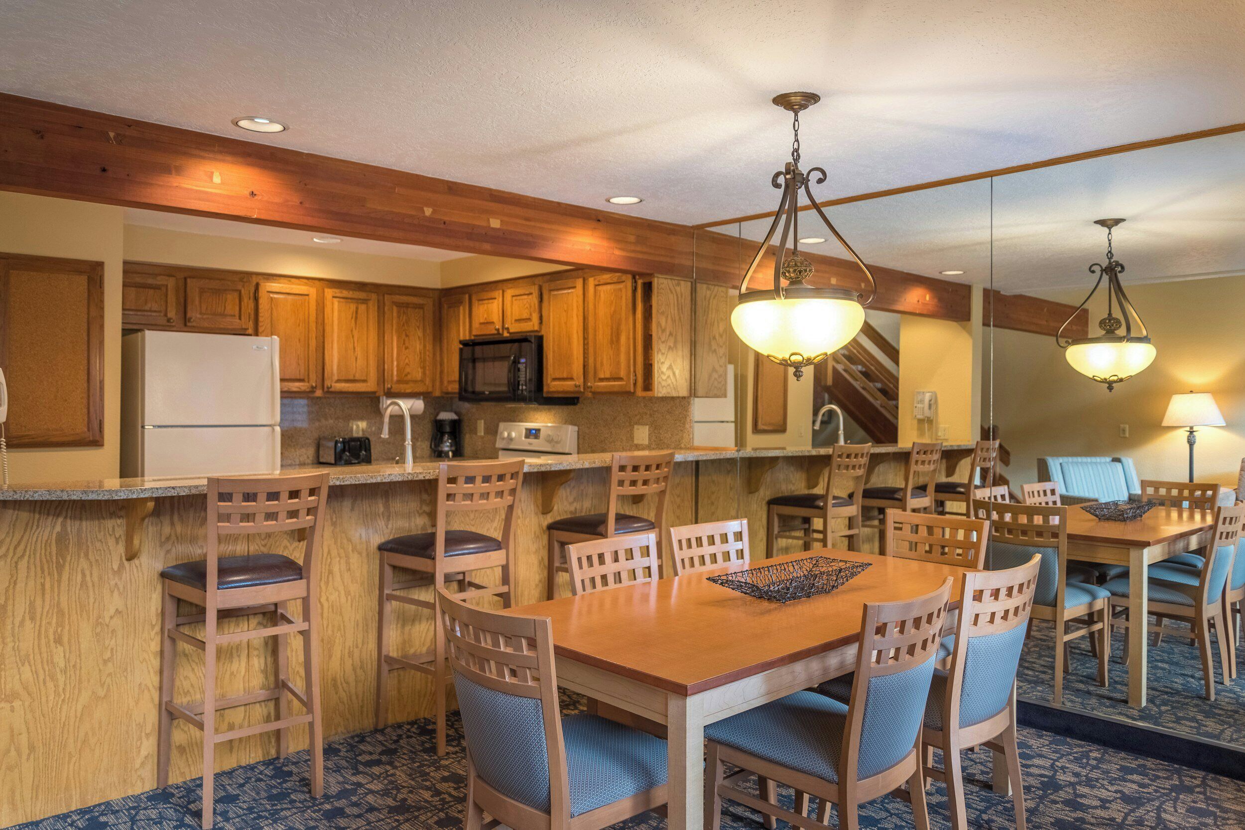 A hotel kitchen with wooden cabinets, a microwave, and a dining area with a table and chairs.