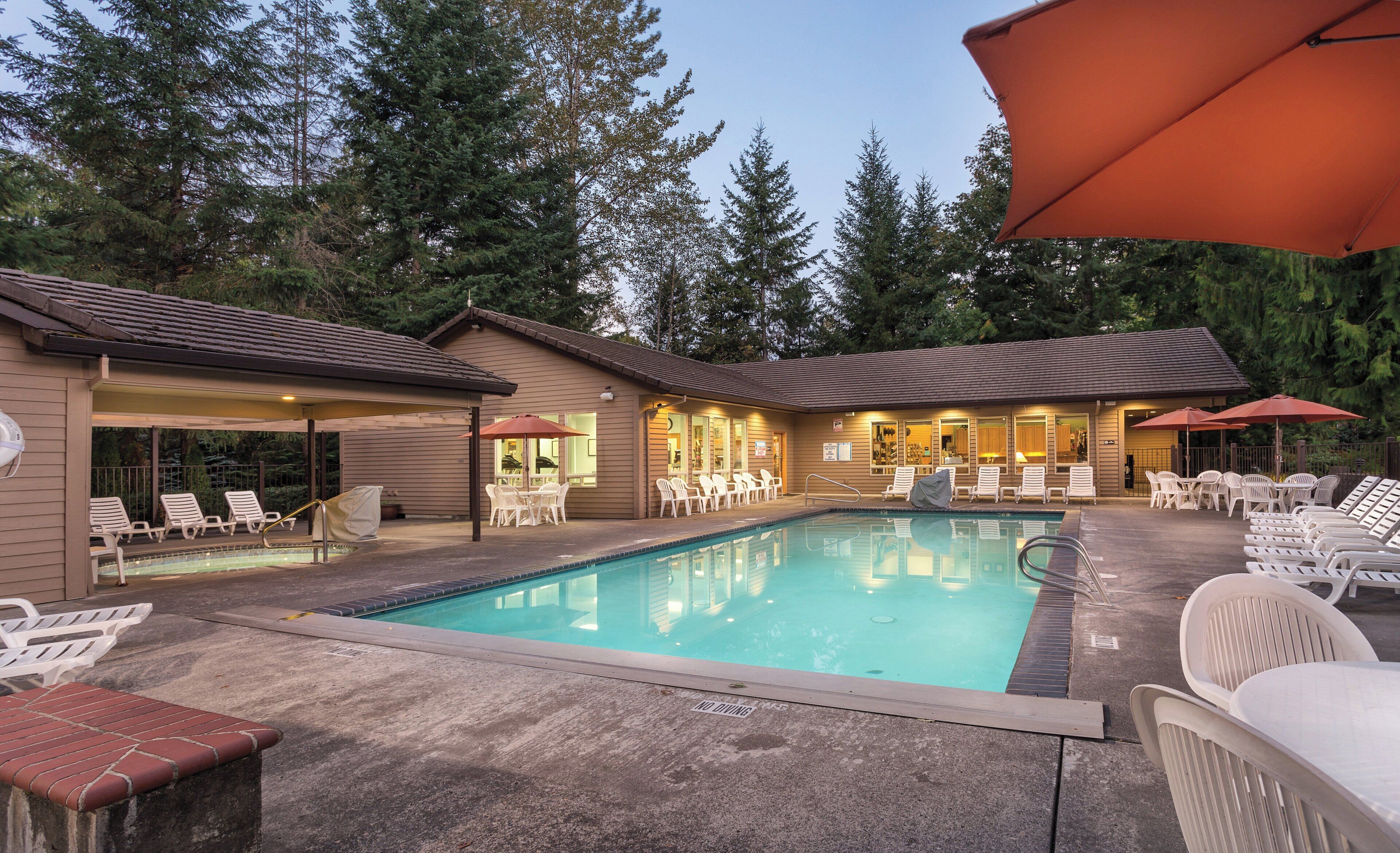A pool area with lounge chairs and umbrellas, surrounded by buildings with a covered patio.