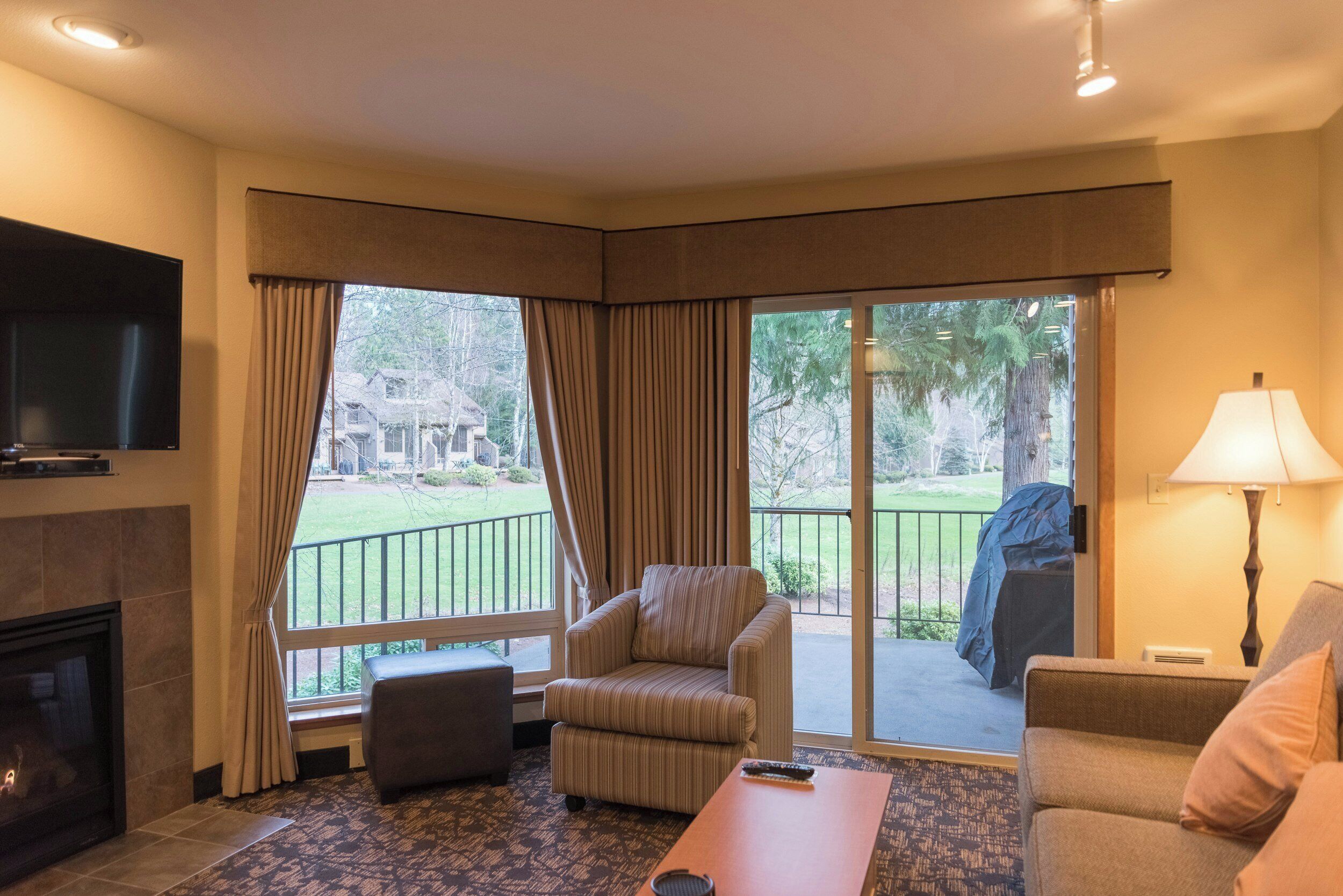 Habitación de hotel con televisión de pantalla plana, chimenea, sillón a rayas, sofá, mesa de centro y vistas al exterior a través de amplios ventanales.