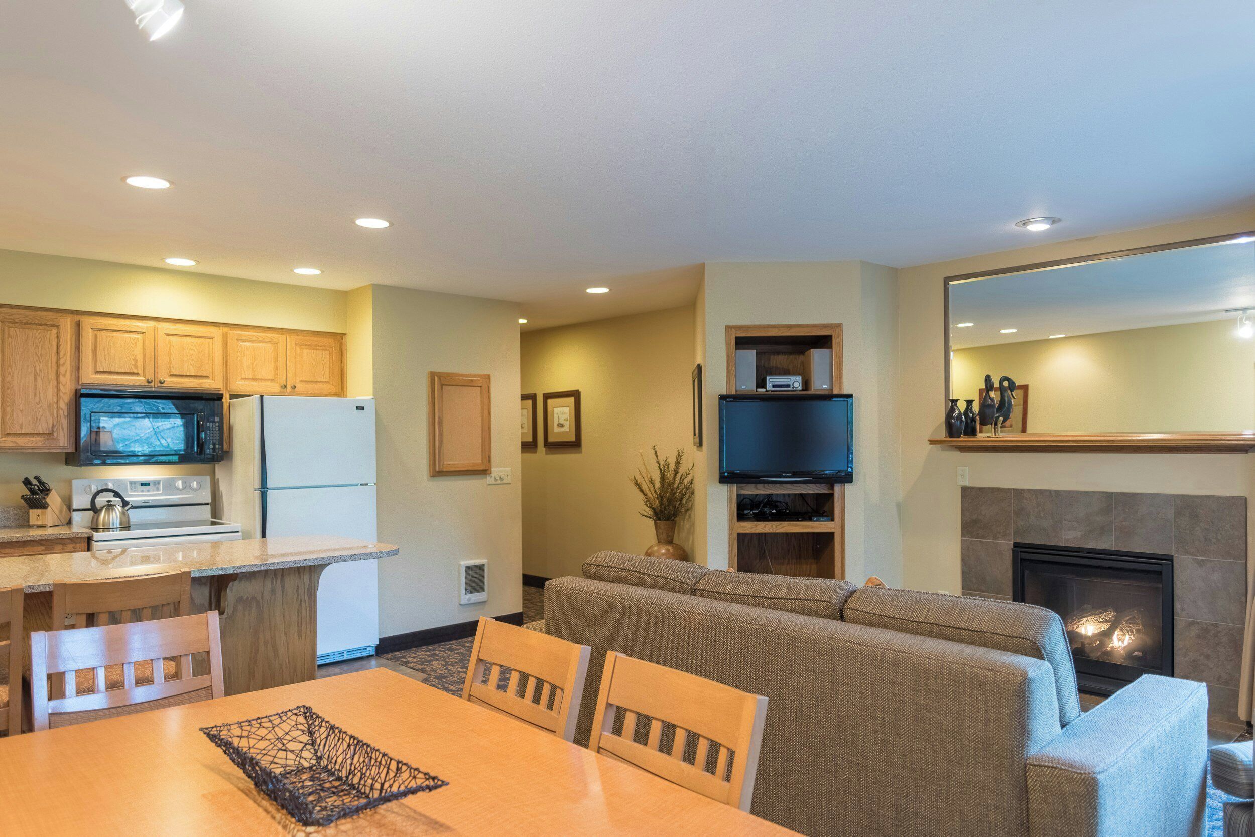 Un espacio habitable compacto con kitchenette, un televisor de pantalla plana, chimenea y zona de estar con sofá y sillones.