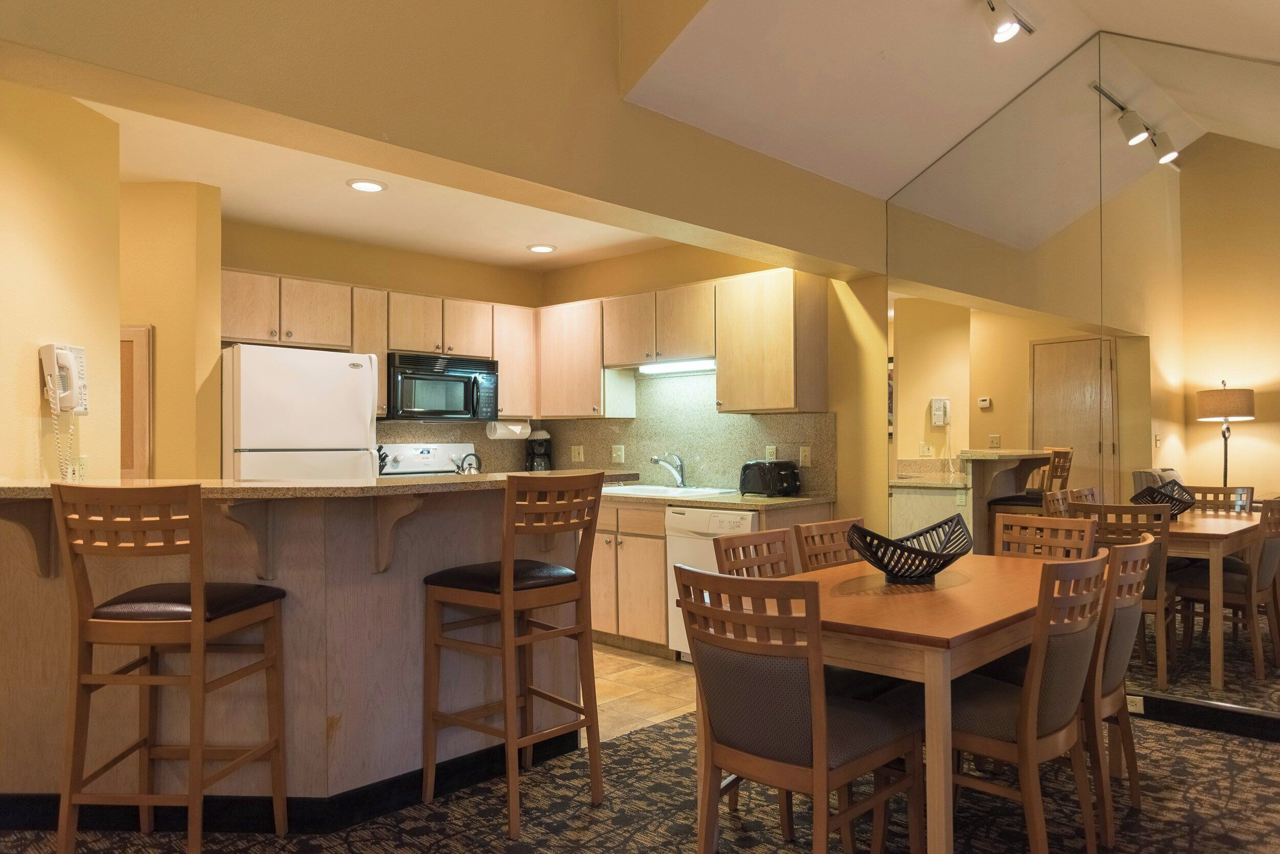 Cocina compacta de hotel con refrigerador, microondas y estufa, un pequeño comedor con mesa y sillas, y una kitchenette separada.