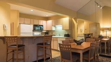 A compact hotel kitchen with a refrigerator, microwave, and stove, a small dining area with a table and chairs, and a separate kitchenette.