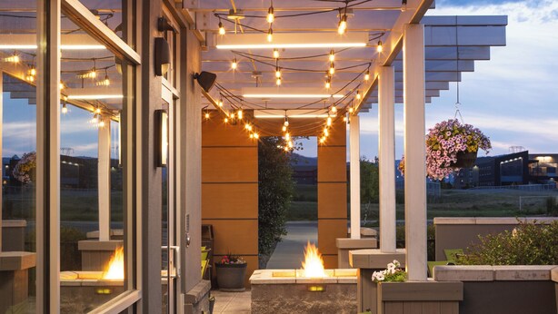 Un patio al aire libre con luces colgantes, sillas verdes y una chimenea.