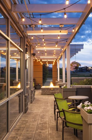 Un patio al aire libre con luces colgantes, sillas verdes y una chimenea.