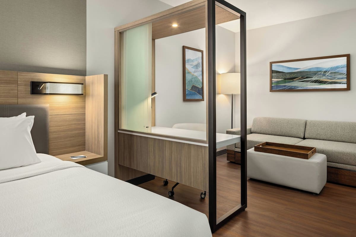 Ett modernt hotellrum med en säng, en soffa, ett skrivbord och en stor spegel.