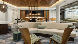 Un vestíbulo de hotel moderno con un amplio sofá modular, dos sillones, una zona de bar y una pantalla de televisión.
