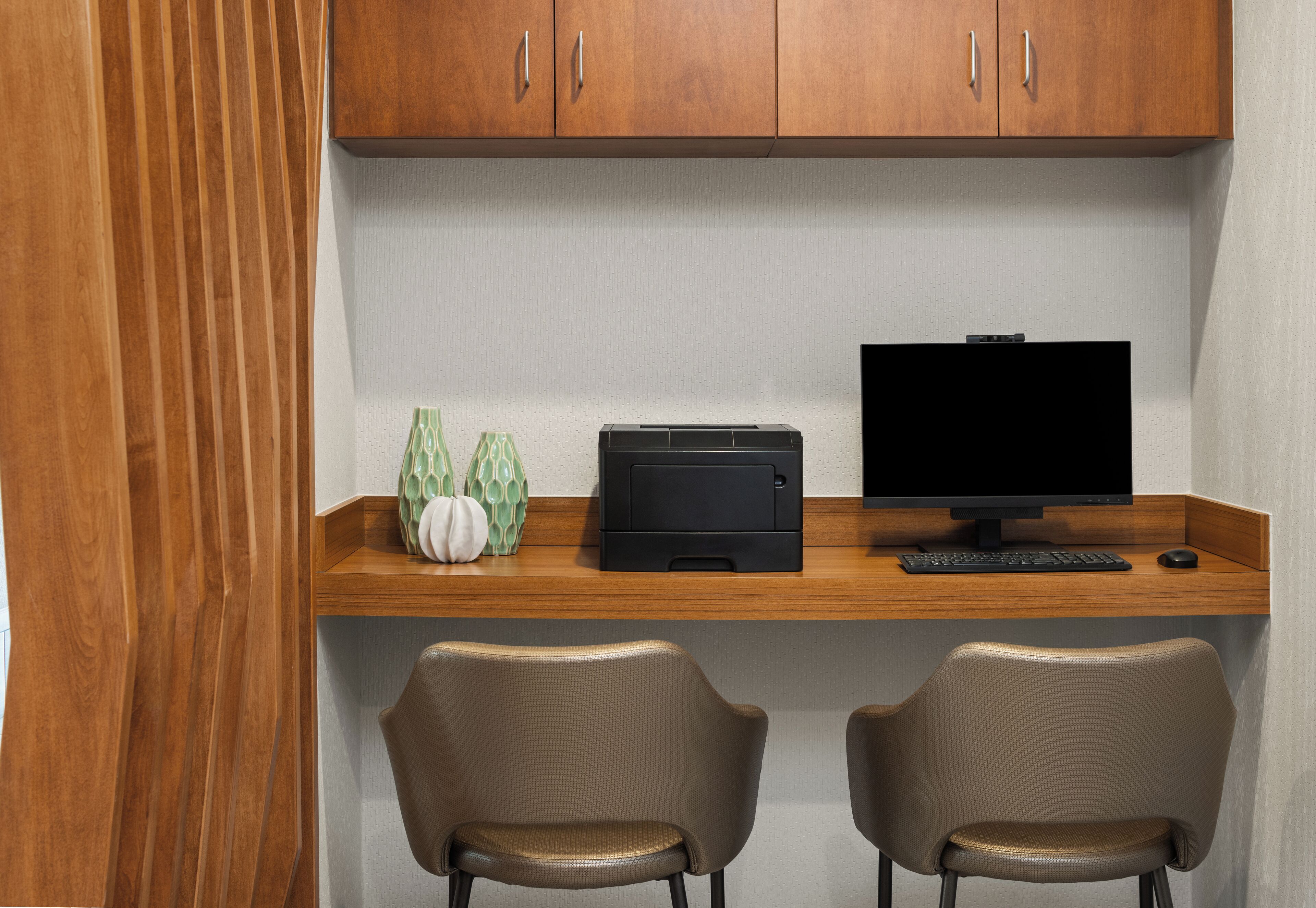 Een werkplek met een houten bureau, twee stoelen, een computer monitor, een printer en decoratieve objecten.