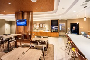 Un hall d’hôtel moderne avec un long comptoir d’accueil, un téléviseur fixé sur un panneau en bois et un coin bar avec des tabourets.