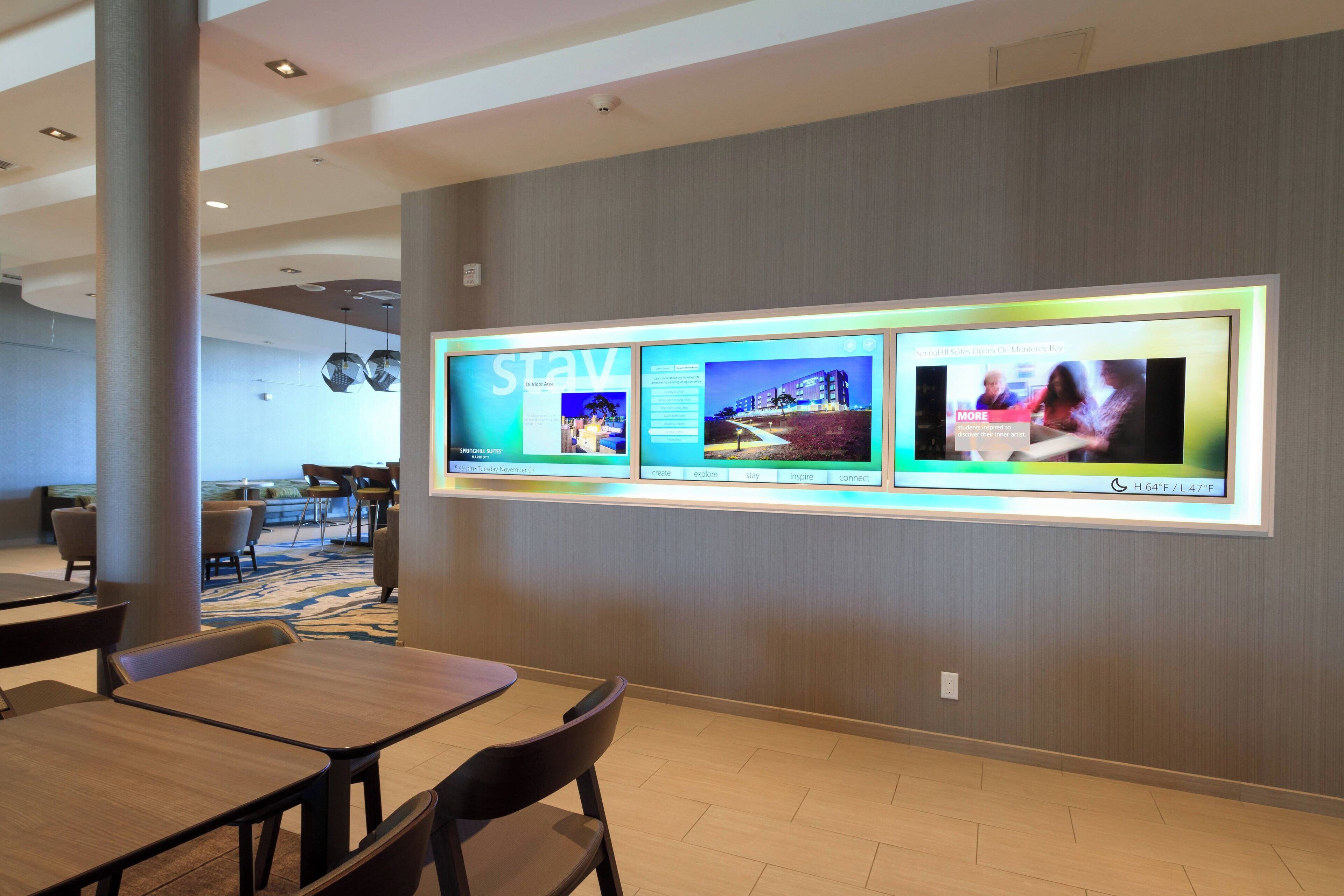 A hotel lobby with a reception area, seating, and a digital display wall.