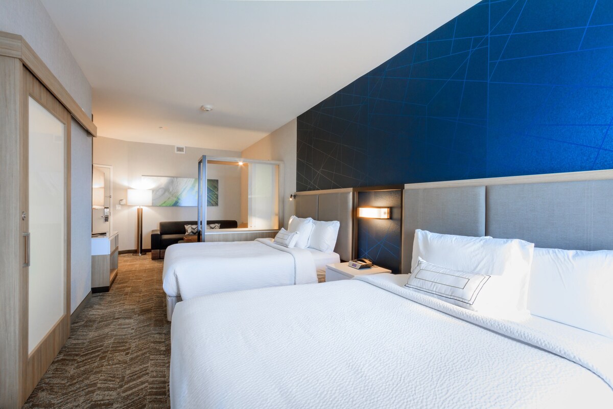 Une chambre d’hôtel avec deux lits, un grand miroir, un bureau et un mur d’accent bleu.