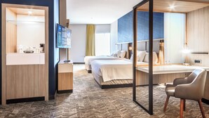 Quarto de hotel moderno com uma cama grande, uma escrivaninha, uma cadeira, uma TV e um espaço para o banheiro.