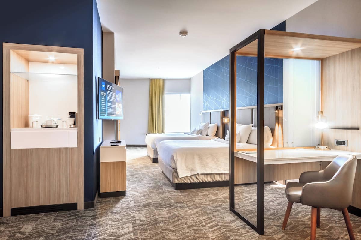 A modern hotel room with a large bed, a desk, a chair, a TV, and a bathroom area.