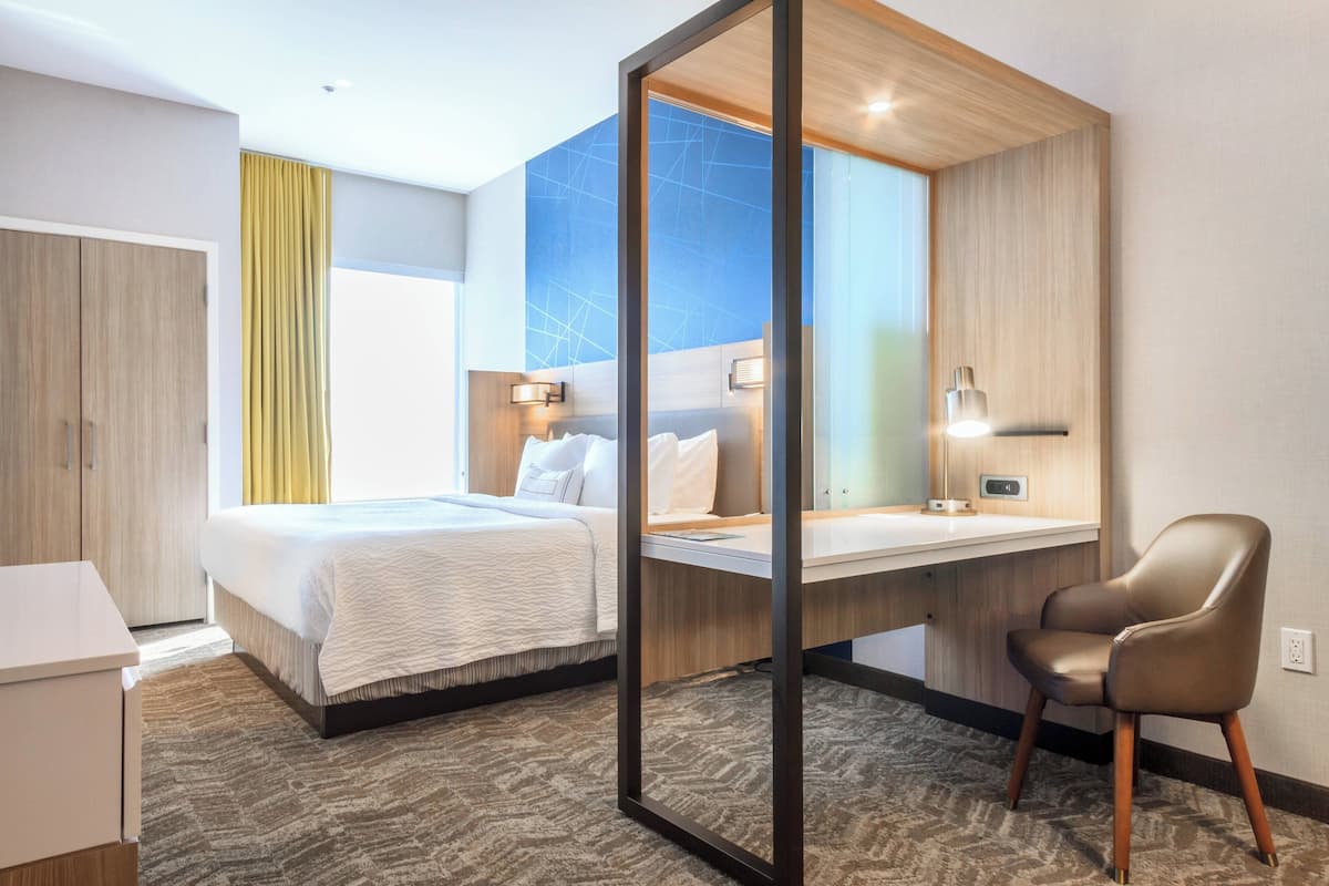 A hotel room with a bed, desk, chair, and a large mirror.