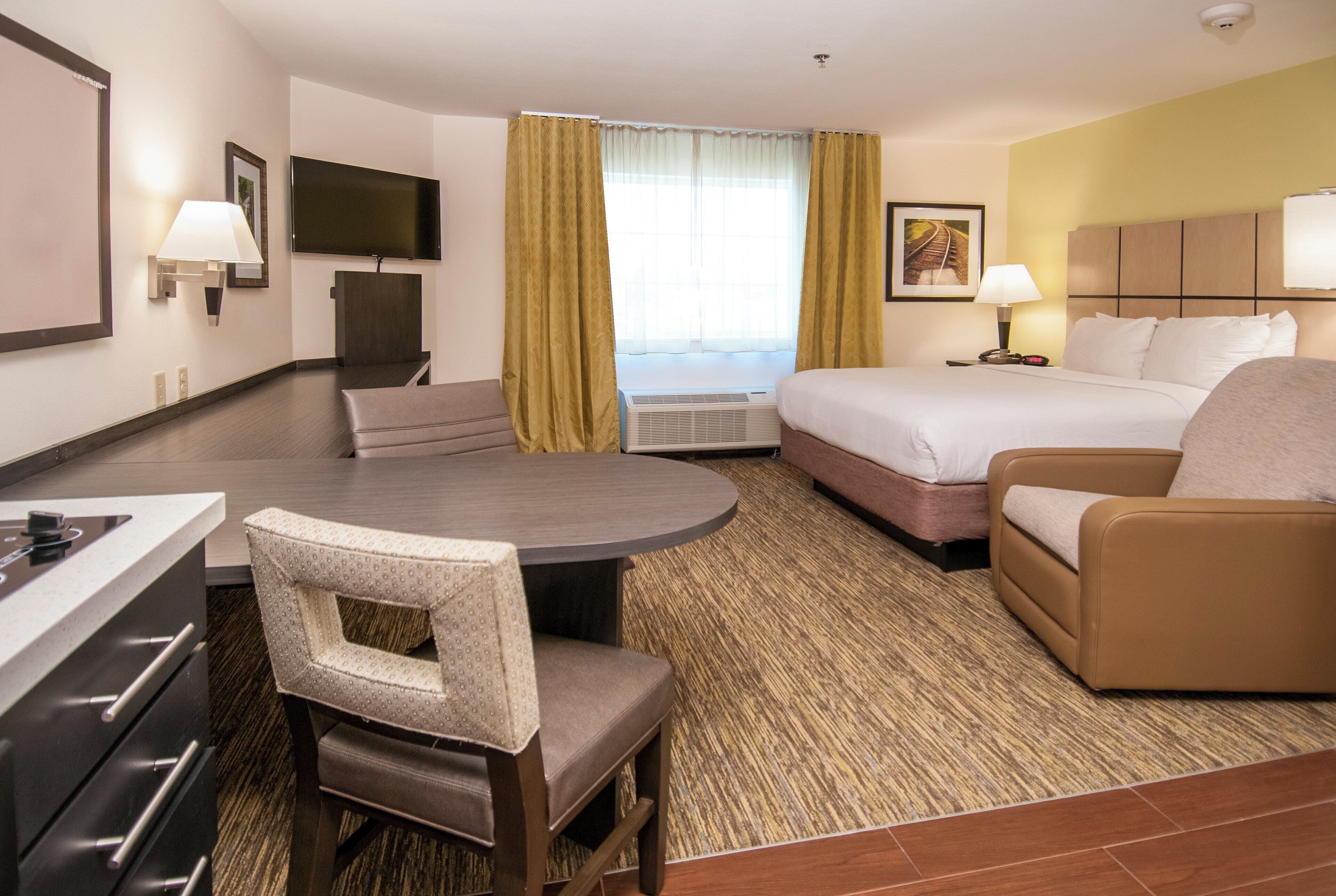 A hotel room with a bed, a sofa, a desk, a chair, a television, and a window with curtains.
