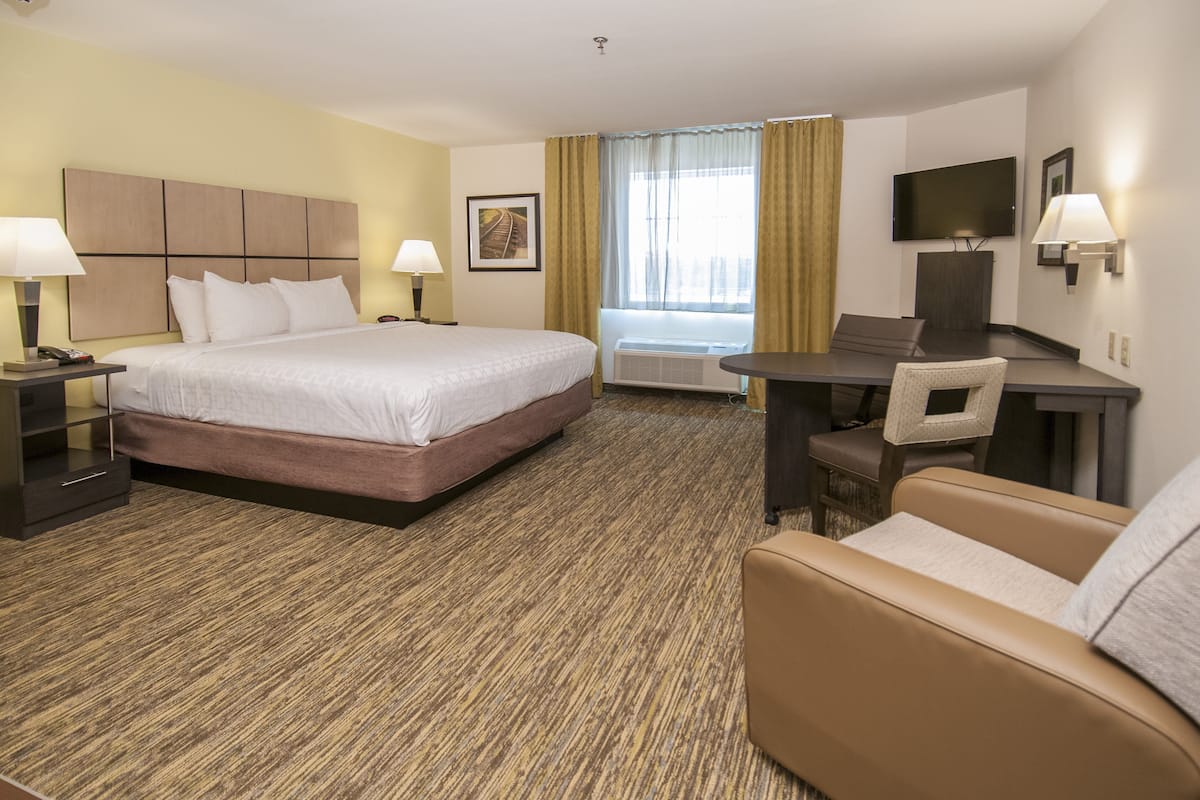 A hotel room with a bed, a desk, a chair, a TV, and an air conditioning unit.