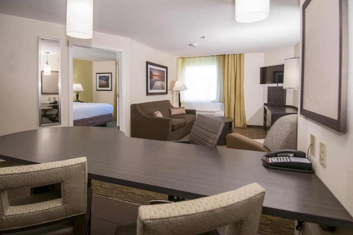 A hotel room with a large conference table, a sofa, a bed, a desk with a lamp, and a TV.
