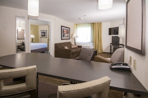 Habitació d'hotel amb una gran taula de conferències, un sofà, un llit, escriptori amb una làmpada i una televisió.