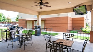 Un espace extérieur aménagé en terrasse, avec des tables et des chaises, un ventilateur de plafond et un téléviseur fixé au mur.