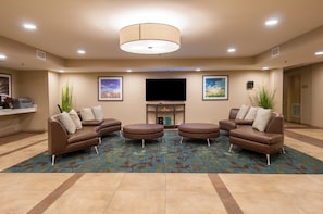 A hotel room with a large flat-screen TV, two sofas, a coffee table, and a patterned carpet. - Candlewood Suites Baton Rouge - College Drive by IHG (Baton Rouge)