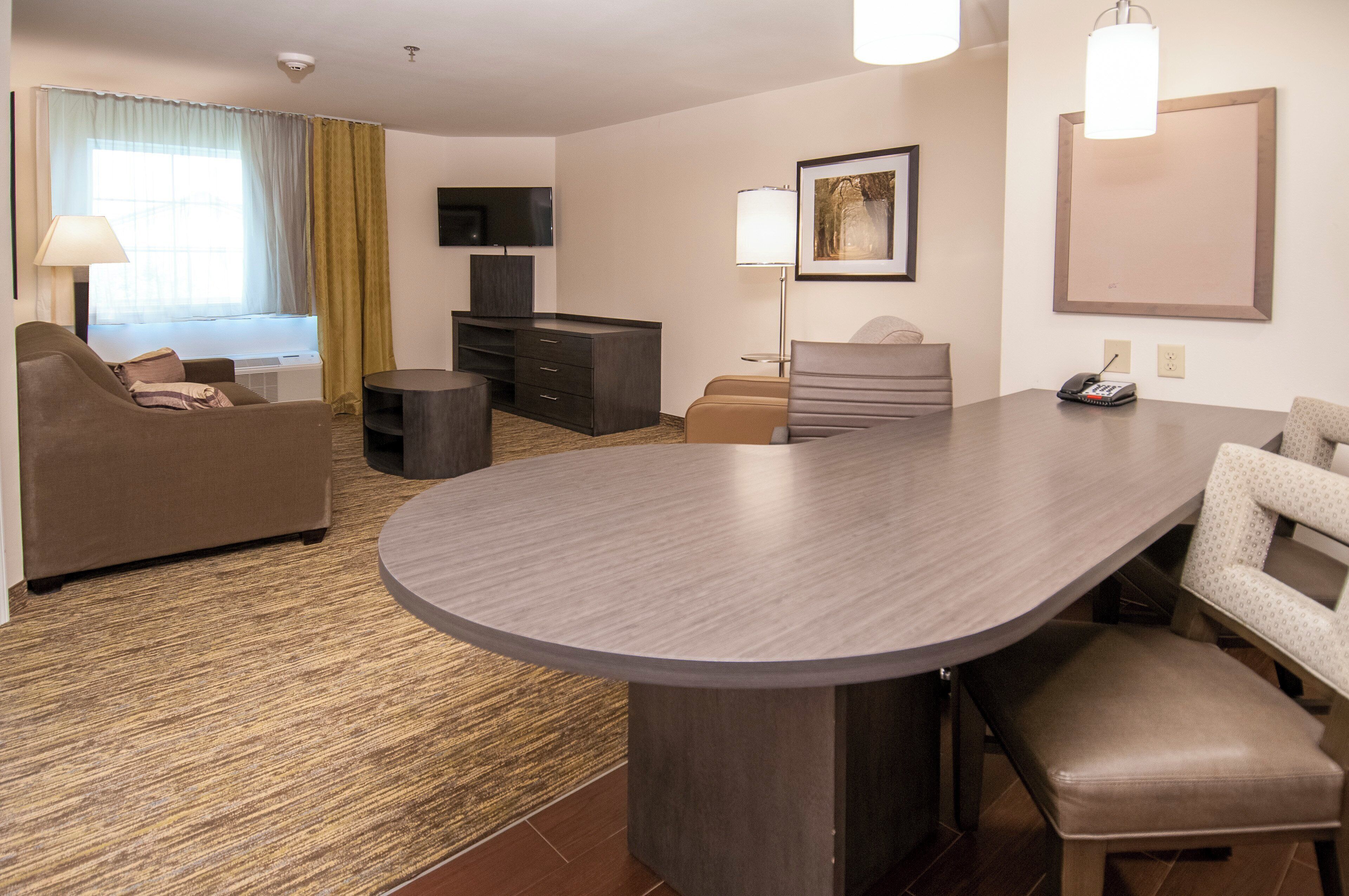 Habitación de hotel con sofá, escritorio, silla, televisor de pantalla plana, lámpara, un cuadro y teléfono.