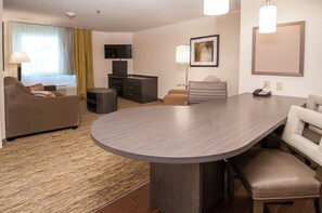 Ein Hotelzimmer mit Sofa, Schreibtisch, Stuhl, Flachbildfernseher, Lampe, Gemälde und Telefon.