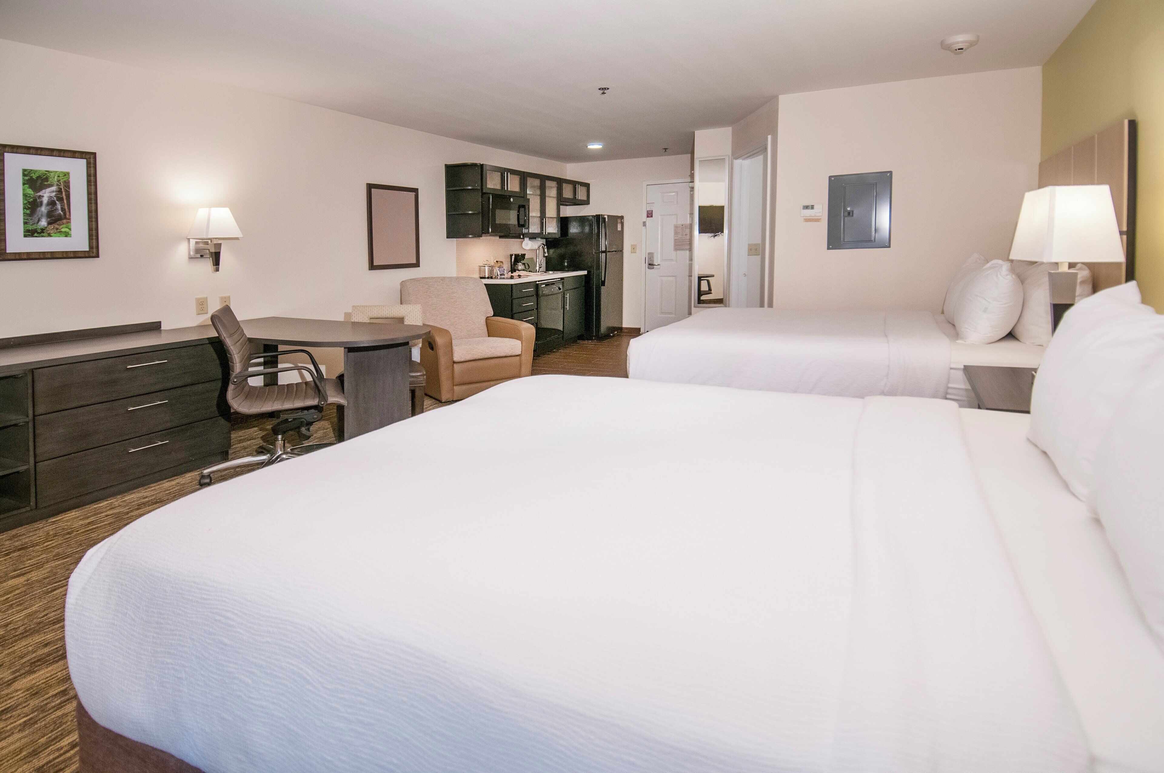 A hotel room with two beds, a desk, a chair, a kitchenette, and a bathroom.