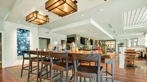 A spacious dining area with a long wooden table and chairs, a kitchen in the background, and pendant lighting. - The Inn at Swarthmore (Swarthmore)