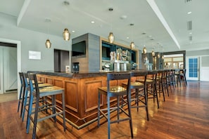A spacious bar area with a long counter and multiple stools, a television mounted on the wall, and a bar stocked with various bottles.