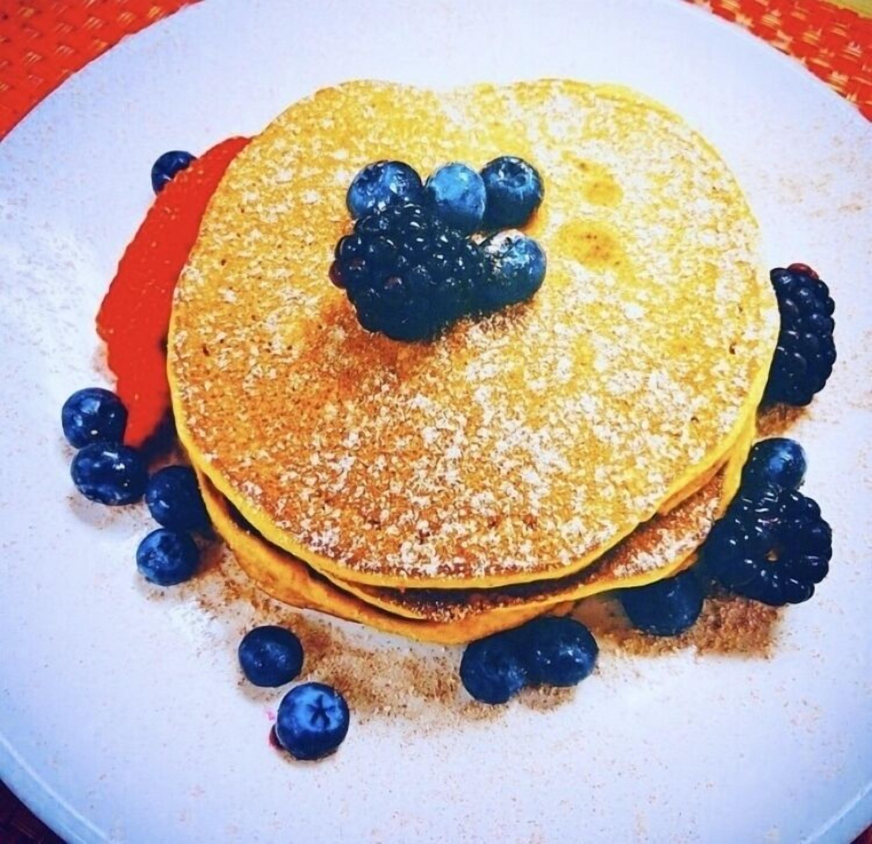 A stack of pancakes with blueberries and a red sauce on a white plate.