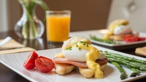 A breakfast plate with eggs benedict, ham, asparagus, and tomatoes.