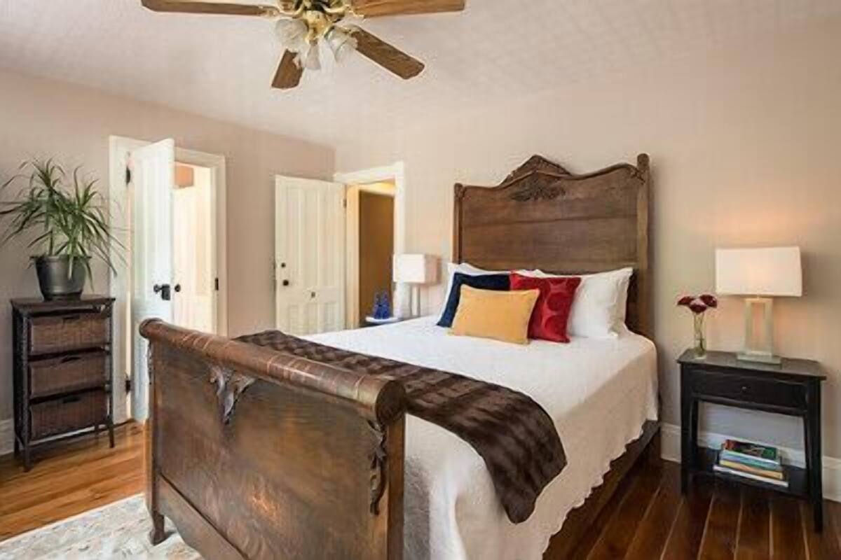 Ein Schlafzimmer mit einem hölzernen Bett, weißen Wänden, einem Deckenventilator und einem Nachttisch mit Lampe und Büchern.