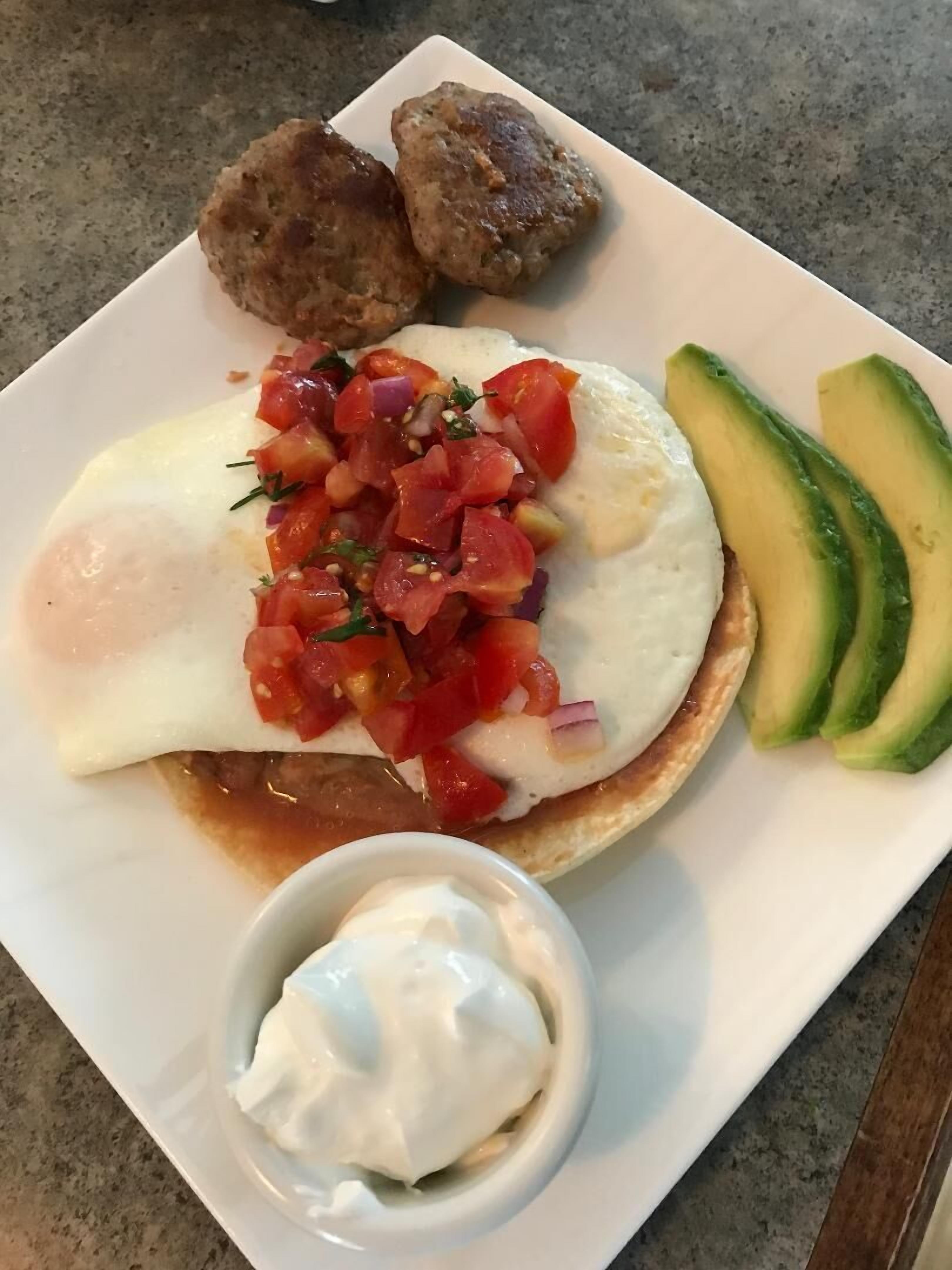 Een ontbijtbord met eieren, plakjes avocado, een tomatensalsa en een klein schaaltje zure room.