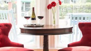 A round table with a wine bottle and glasses, flanked by two red chairs, in a room with large windows and a view of buildings outside.