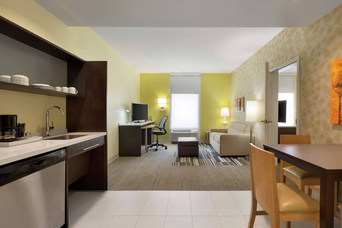 A compact hotel room with a kitchenette, a dining area, and a seating space.