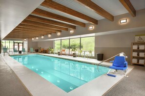 Una piscina interior con vigas de madera, ventanas amplias y una silla elevadora para la piscina.