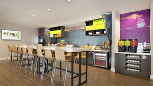 Ein moderner Hotel-Speisebereich mit einem langen Gemeinschaftstisch, Stühlen und einer Kaffeestation.