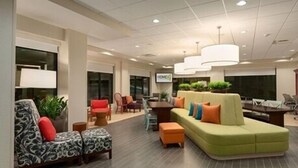 Eine moderne Lobby mit einem grünen Sofa, einem gemusterten Sessel und einem Essbereich mit Tisch und Stühlen.