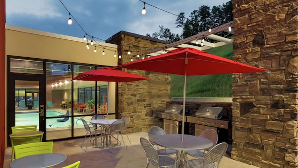 Ein Außenbereich mit einer Terrasse, Steinmauern, einem Grill sowie grünen Metallstühlen und -tischen.