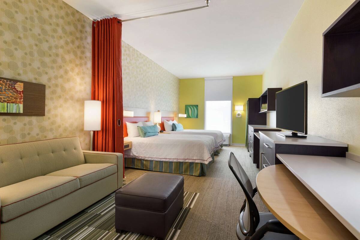 A hotel room with a sofa, a bed, a desk, and a television.