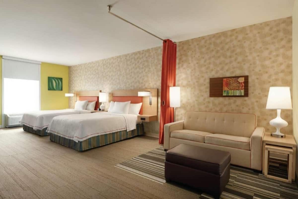 A hotel room with two beds, a sofa, a small table, and a window.