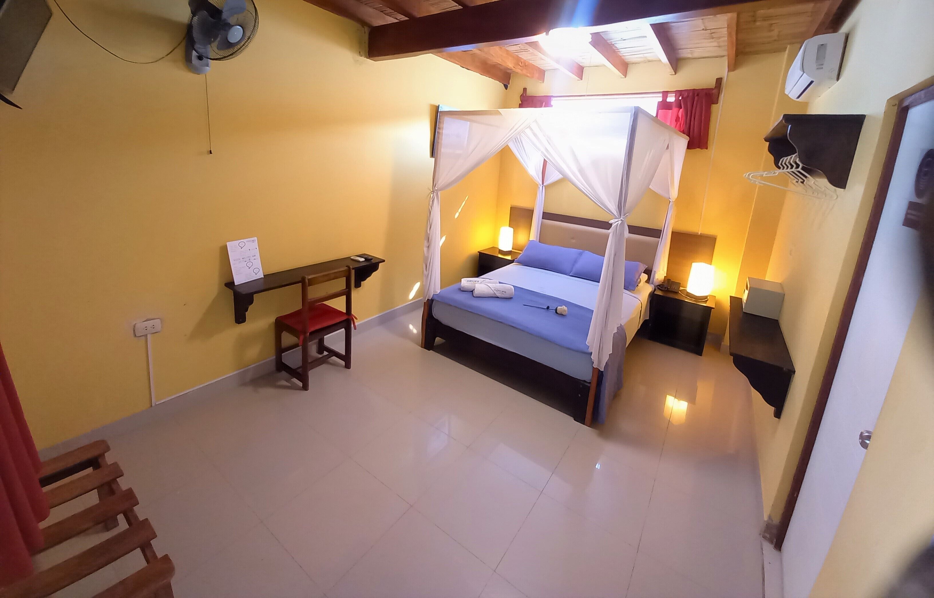 Une chambre à coucher avec un lit sous un dais, des tables de chevet avec des lampes, un petit bureau et une chaise.