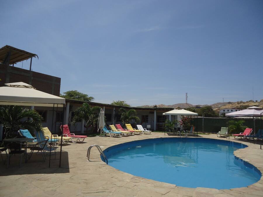 Piscina com espreguiçadeiras e guarda-sóis, rodeada por um edifício com telhado ladrilhado.