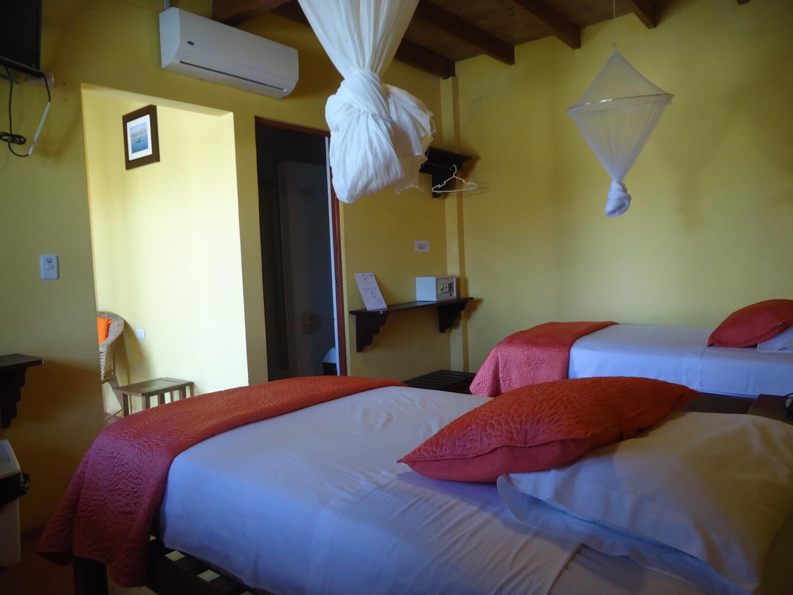 A room with two beds, each with a red pillow, a mosquito net, and a small table with a lamp.