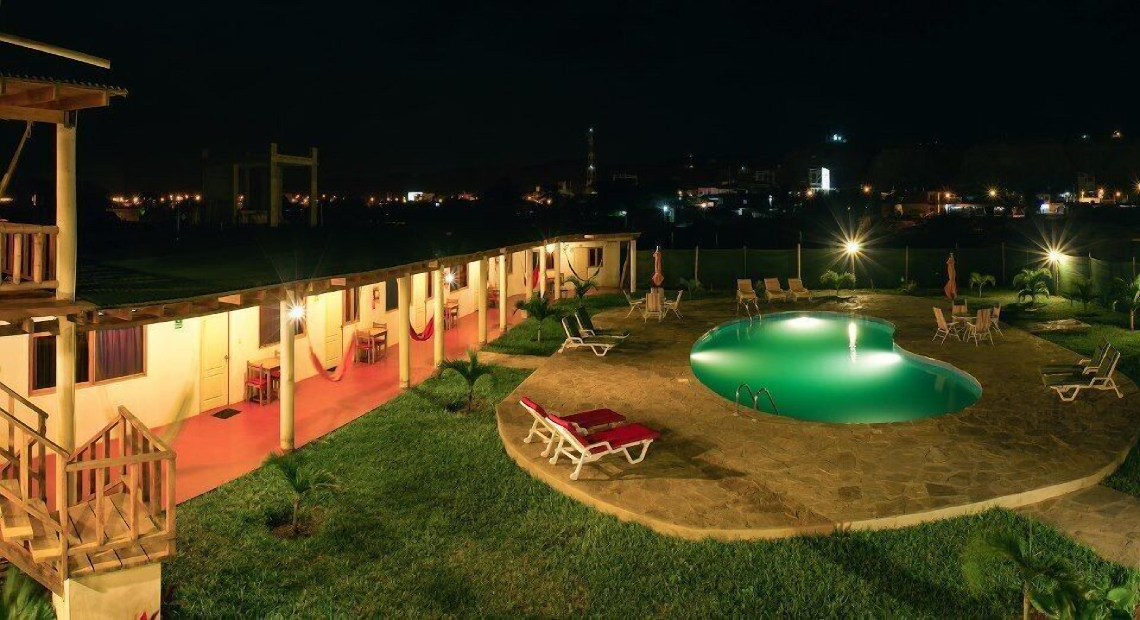 Un hôtel doté d’une piscine, de chaises longues et d’un espace extérieur couvert pour la soirée.