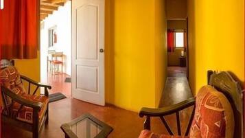 Una habitación con paredes amarillas, una puerta blanca y dos sillas de madera con cojines estampados.