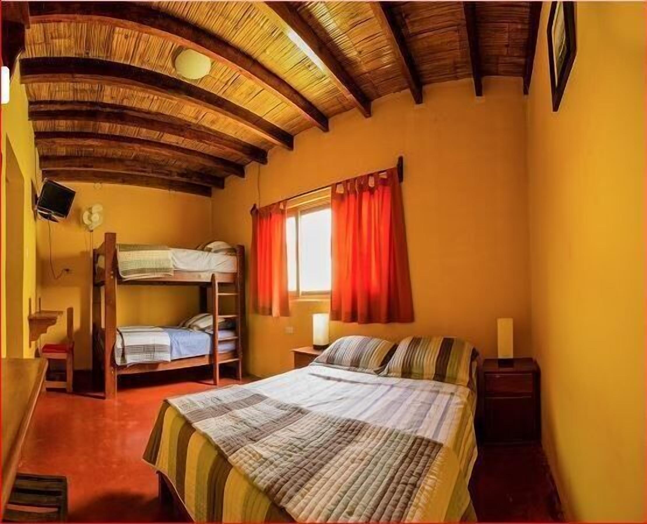 A room with a bunk bed, a single bed, a desk, and a window with curtains.