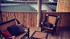 A wooden deck with wicker furniture and a view of a beach and thatched-roof buildings. - Mancora y Sol (Máncora)